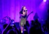woman in green sparkly dress sings on stage with purple backlights