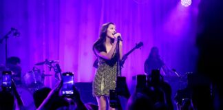 woman in green sparkly dress sings on stage with purple backlights