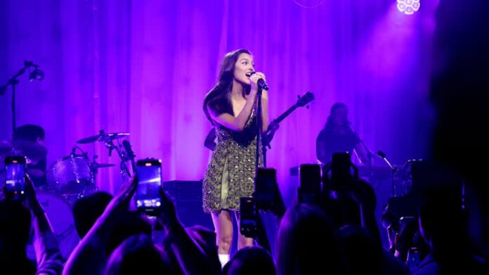 woman in green sparkly dress sings on stage with purple backlights