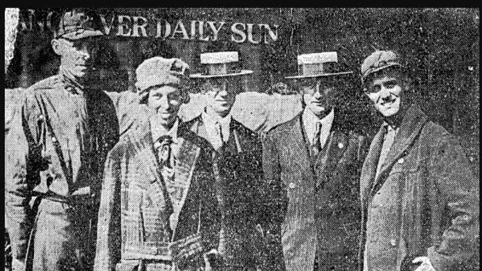 A news paper photo of five people posing in front of a newspaper office.