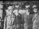A news paper photo of five people posing in front of a newspaper office.