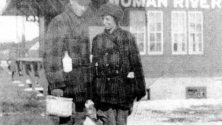 A man and woman are shown in a grainy photo standing in front of a building with the name Woman River.