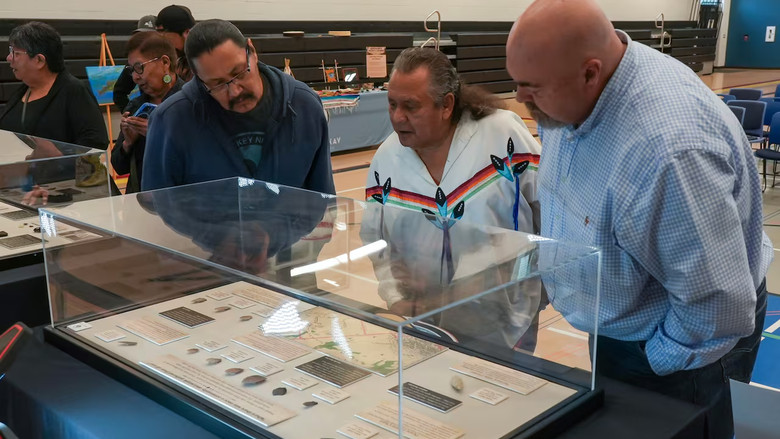 A group of three men look at artifacts in a display case.