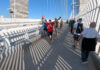 A man in a t-shirt with his arms in the air in a welcoming stance leads a row of people walking down the path while another row walks in the other direction.
