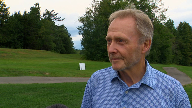 A senior wearing a blue golf shirt is shown at a golf course.