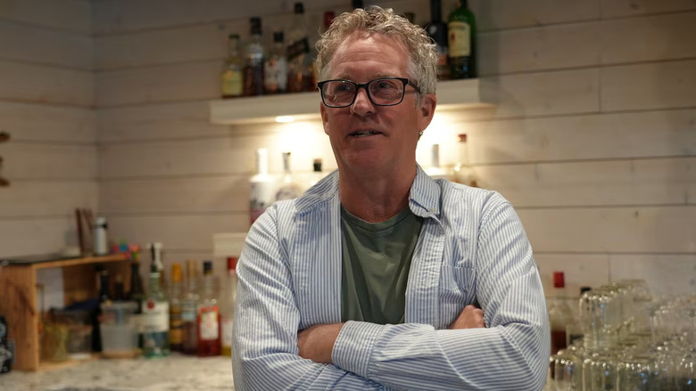 A man standing arms crossed behind a bar.