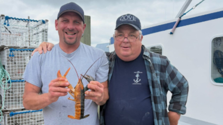 Two men, one younger and one older, posing with a lobster that is half dark blue and half orange.