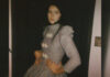 A young woman with dark hair and a long dress poses for the camera in a promotional photo.