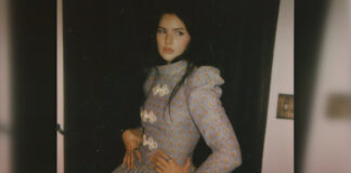 A young woman with dark hair and a long dress poses for the camera in a promotional photo.