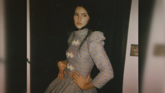 nov01-featured A young woman with dark hair and a long dress poses for the camera in a promotional photo.
