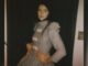 A young woman with dark hair and a long dress poses for the camera in a promotional photo.
