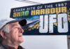 A man is shown in front of a billboard that says 'Crash site of the 1967 Shag Harbour UFO.'