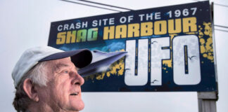 A man is shown in front of a billboard that says 'Crash site of the 1967 Shag Harbour UFO.'