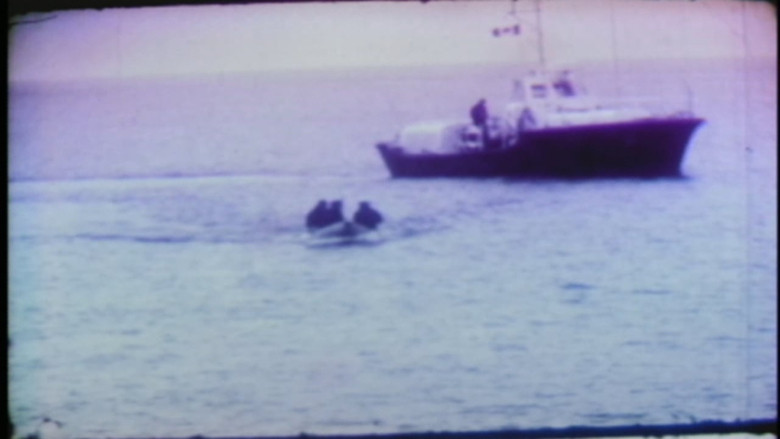 A black and white photo shows three people on a speedboat and a larger boat searching the waters off Shag Harbour, N.S., in October 1967.